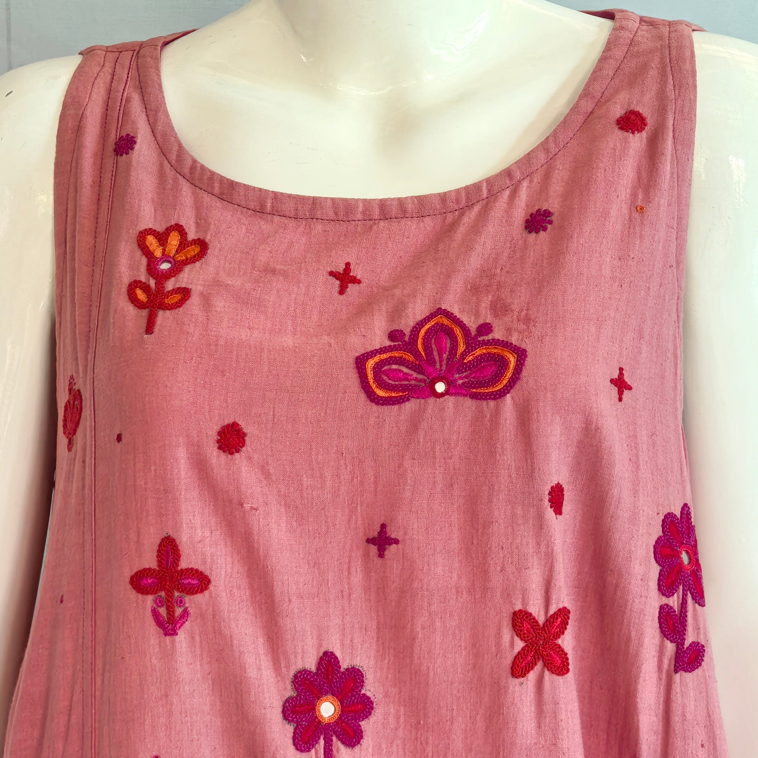 Pink sleeveless top with floral embroidery on a mannequin against a light blue background